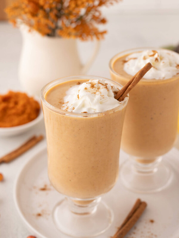Two glasses filled with pumpkin pie smoothie topped with whipped cream.