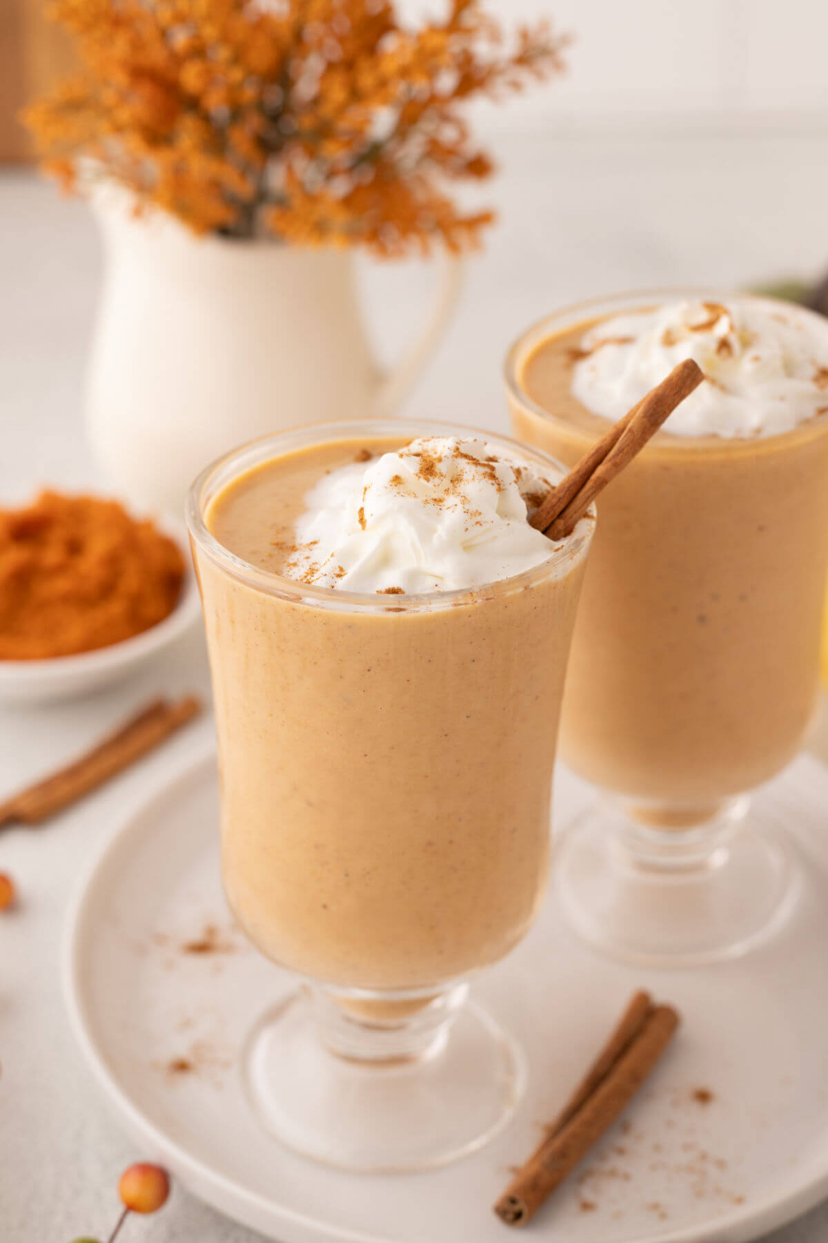 Two glasses filled with pumpkin pie smoothie topped with whipped cream.