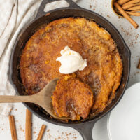 A cast iron skillet with skillet pumpkin cobbler and a dollop of vanilla ice cream on top.