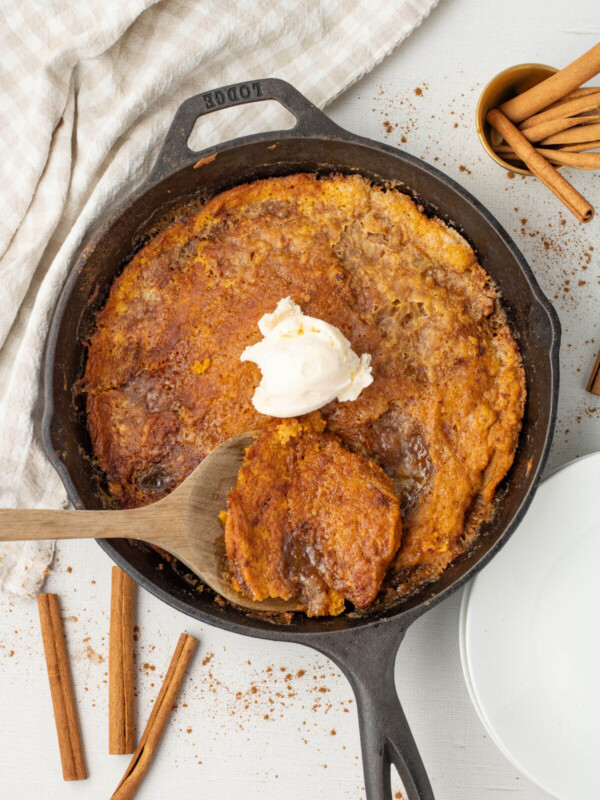 A cast iron skillet with skillet pumpkin cobbler and a dollop of vanilla ice cream on top.