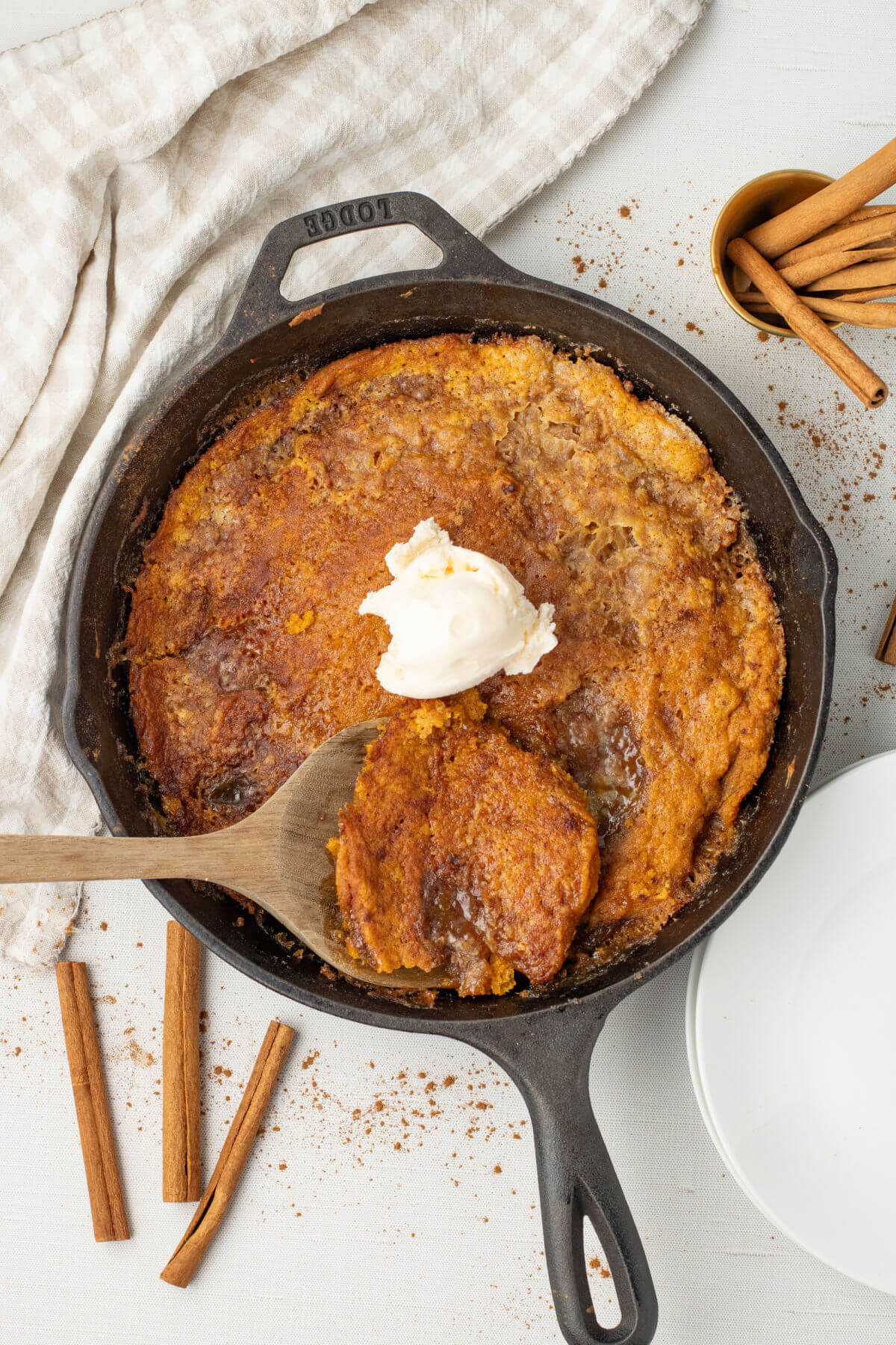 A cast iron skillet with skillet pumpkin cobbler and a dollop of vanilla ice cream on top.
