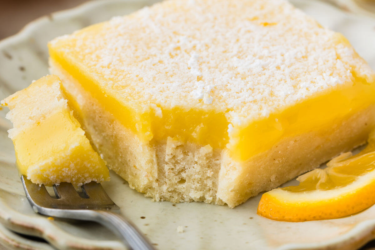 Sourdough lemon bar on a plate with a bite taken out of it.