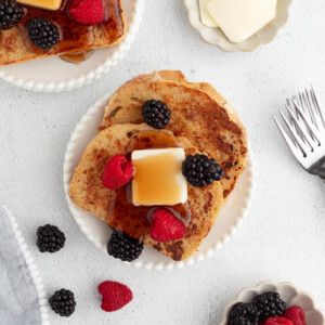 Sourdough French toast on plates with butter, maple syrup, and berries.