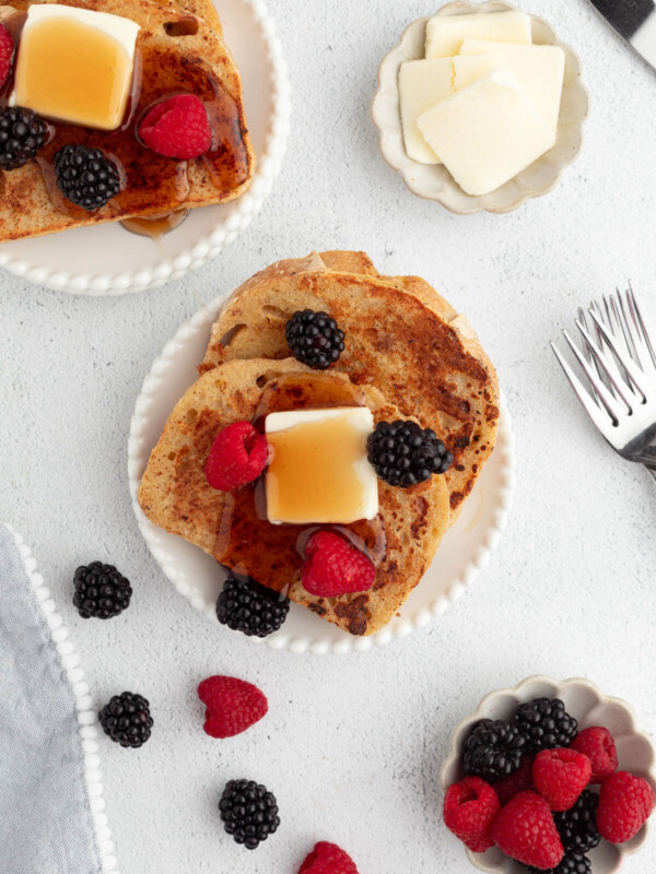 Sourdough French toast on plates with butter, maple syrup, and berries.