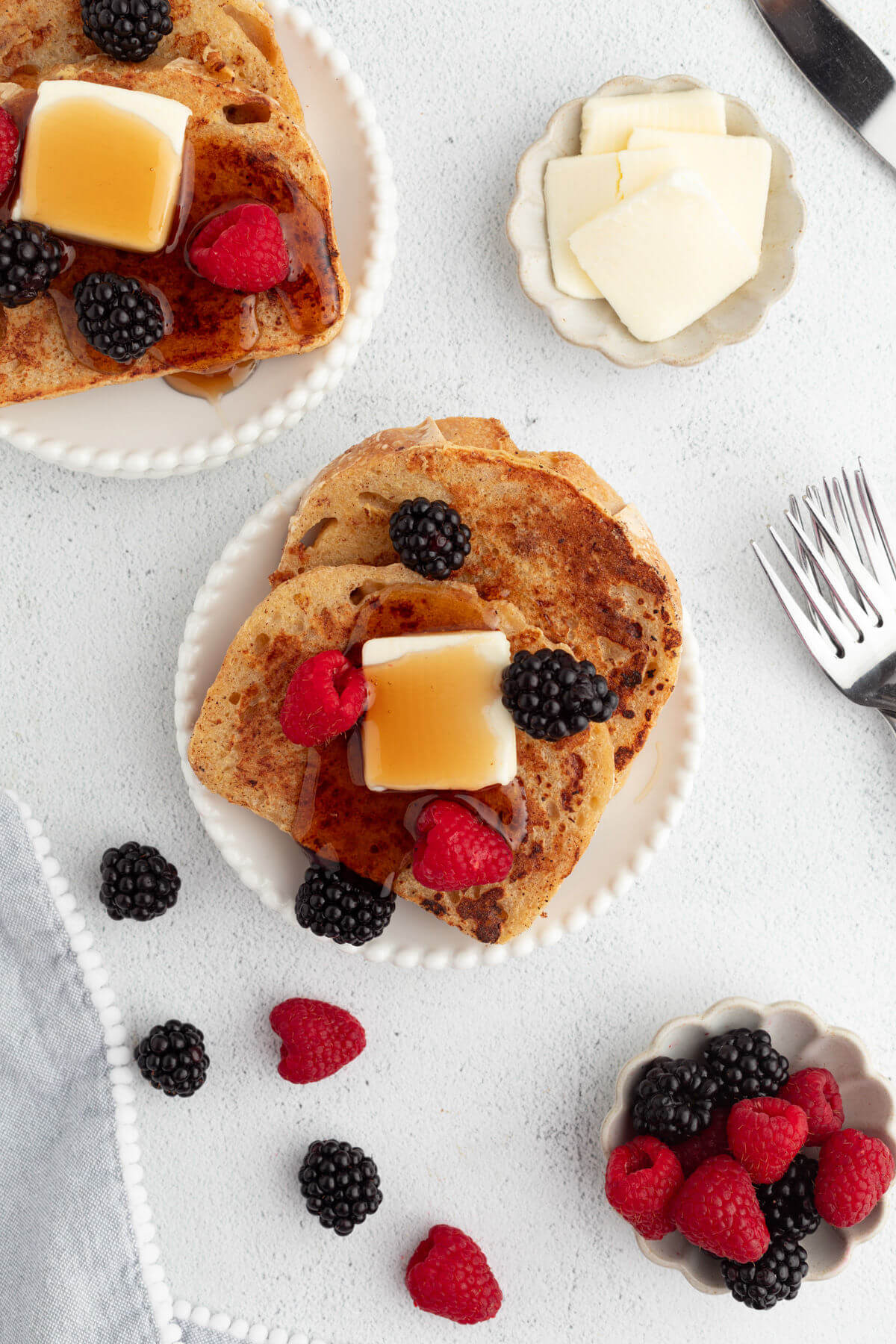 Sourdough French toast on plates with butter, maple syrup, and berries.