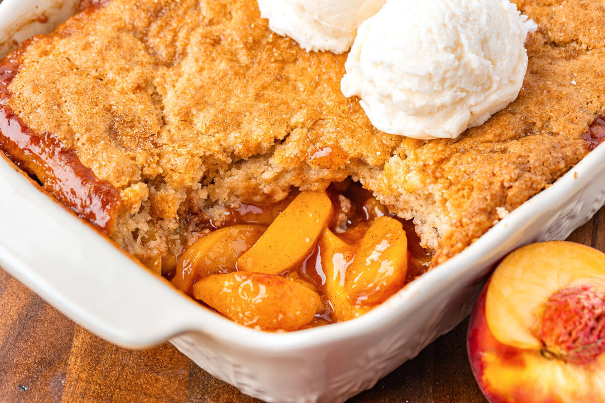 Sourdough peach cobbler in a baking dish with vanilla ice cream on top.