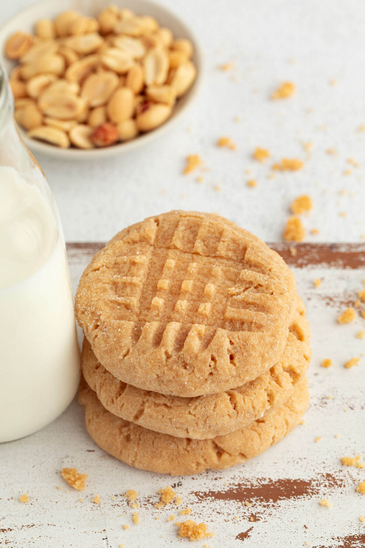 Three sourdough peanut butter cookies next to a glass bottle of milk.