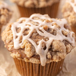 Sourdough pumpkin muffins with crumble topping and cinnamon glaze on parchment paper.