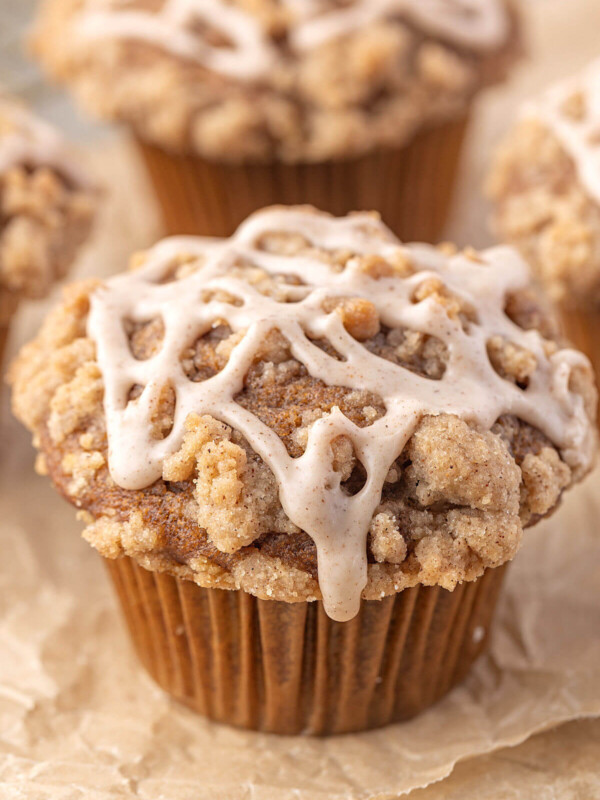 Sourdough pumpkin muffins with crumble topping and cinnamon glaze on parchment paper.