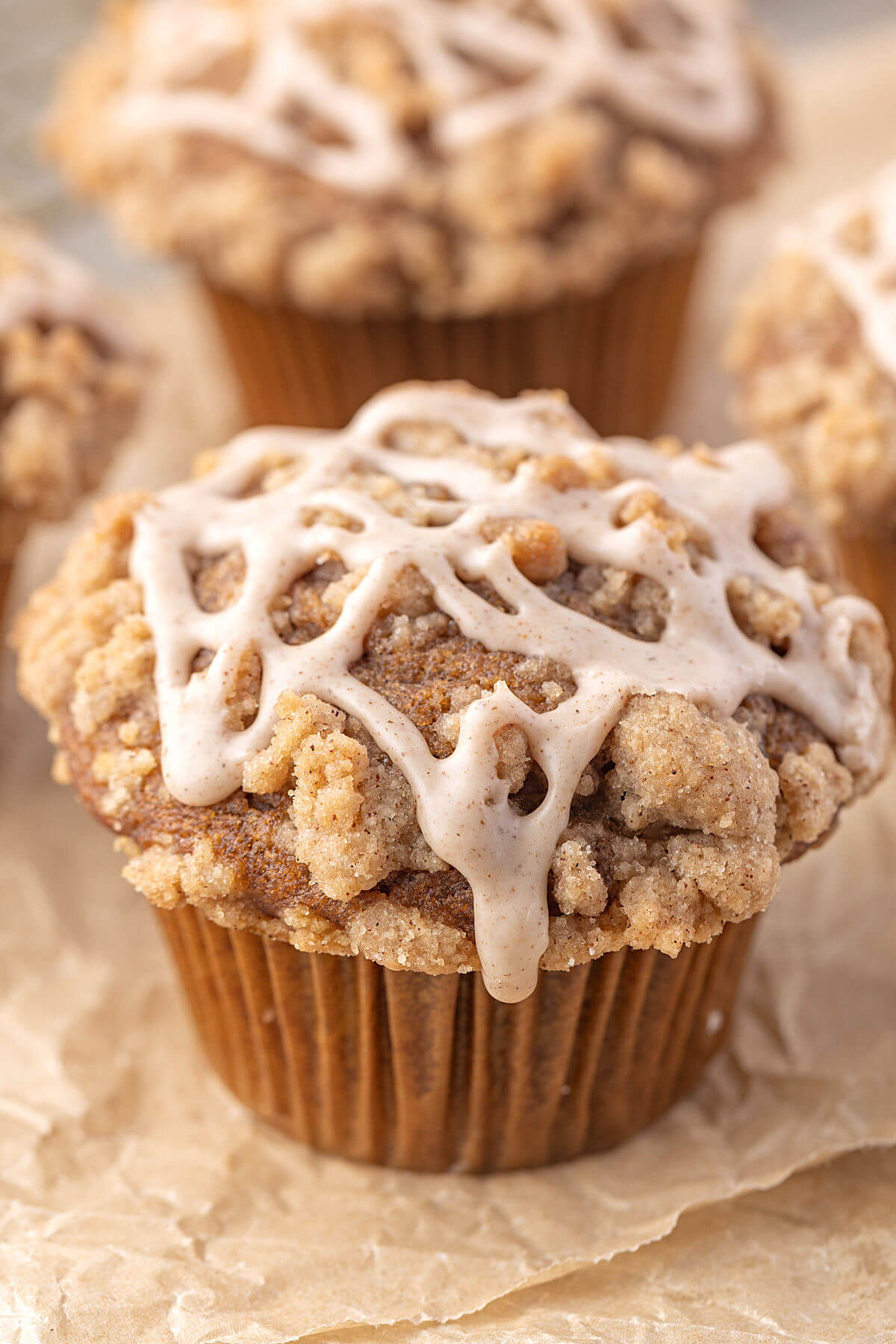 Sourdough pumpkin muffins with crumble topping and cinnamon glaze on parchment paper.