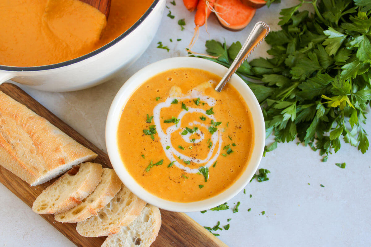 Sweet potato and carrot soup in a serving bowl next to a Dutch oven filled with soup.