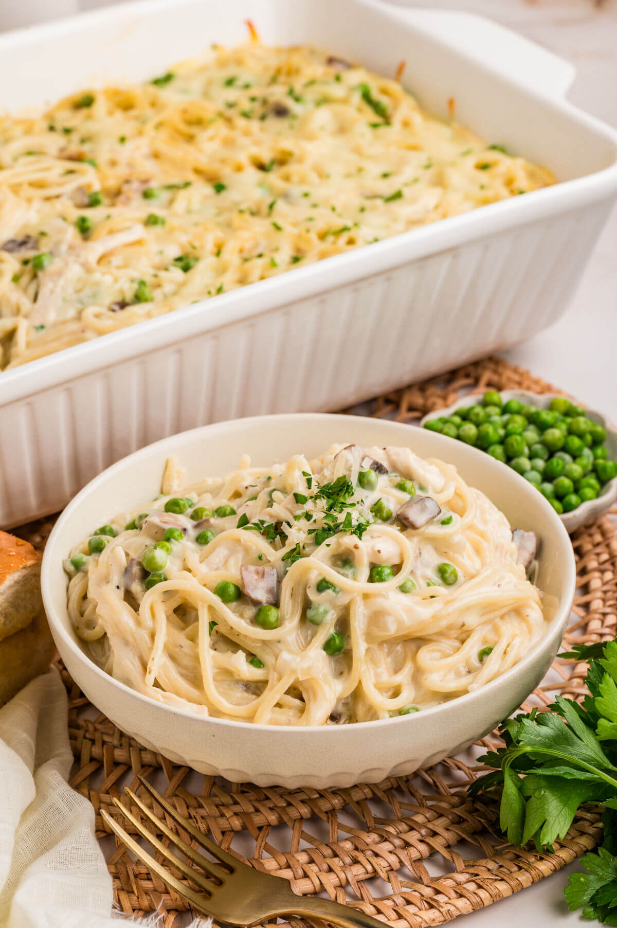 A bowl of turkey tetrazzini next to a baking dish filled with turkey tetrazzini casserole.