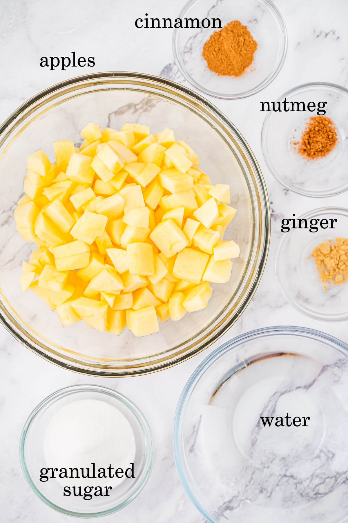 Ingredients for applesauce in small bowls with text overlay labeling each ingredient.