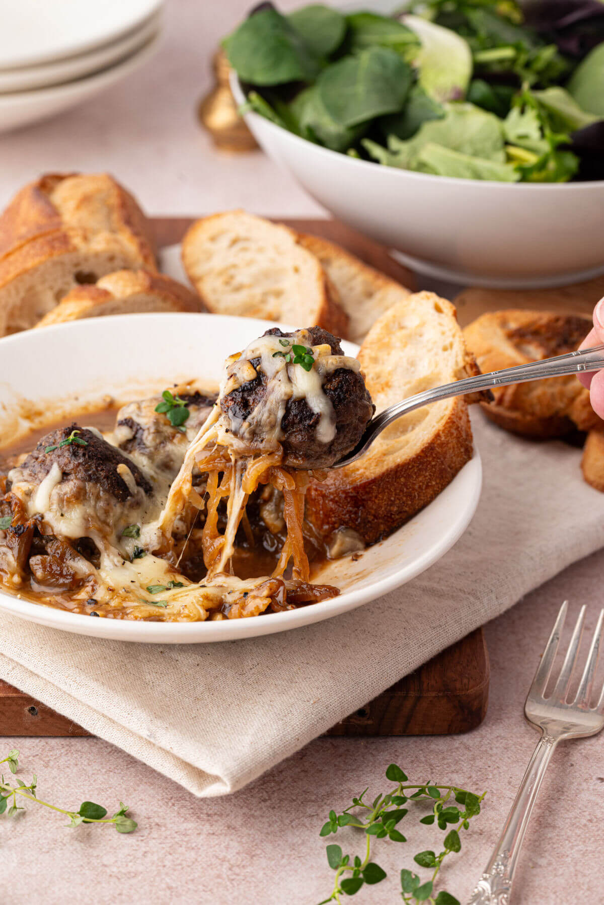 French onion meatballs on a plate with melted cheese, crusty French bread, and a salad.