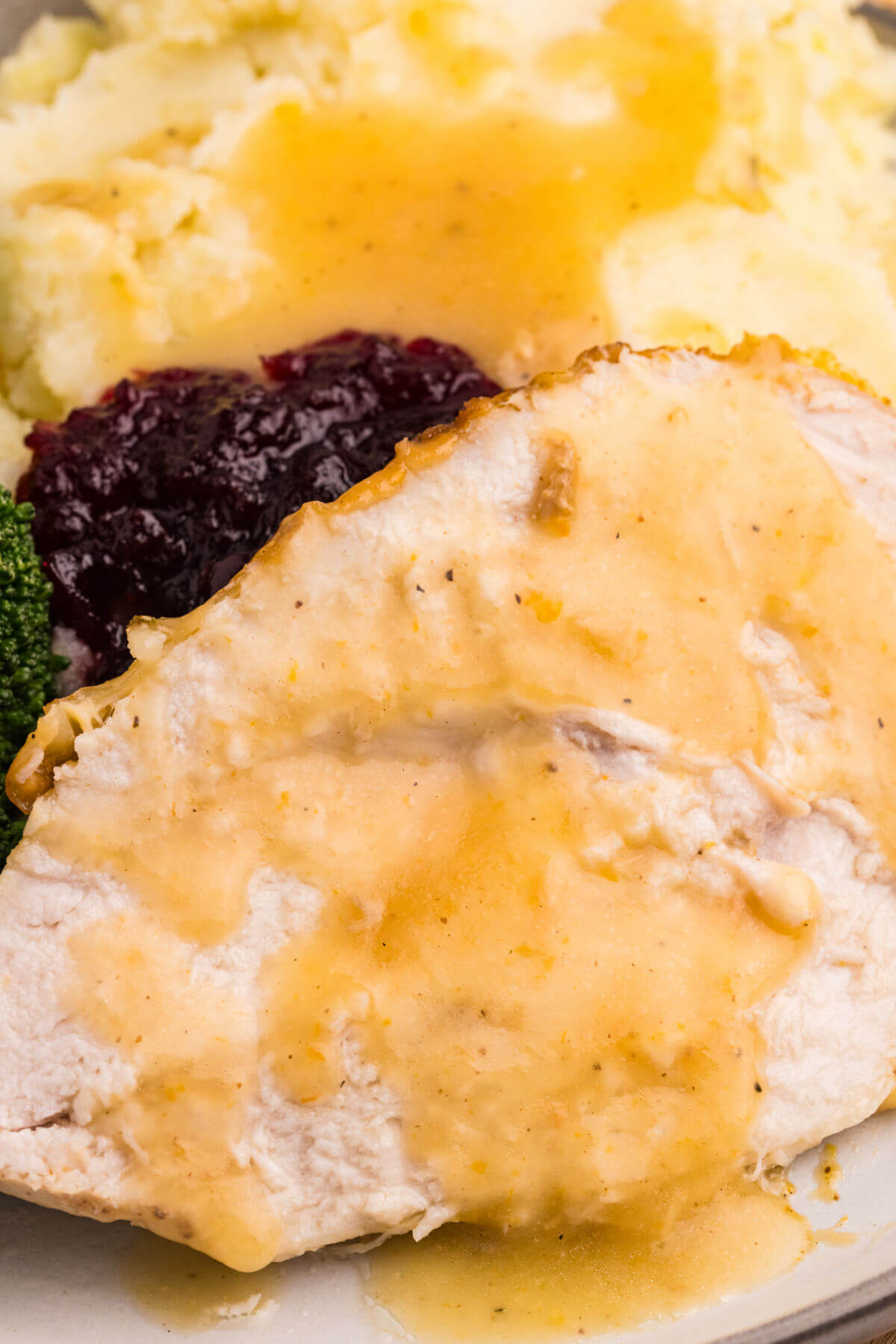 Sliced honey glazed turkey with gravy on a plate.