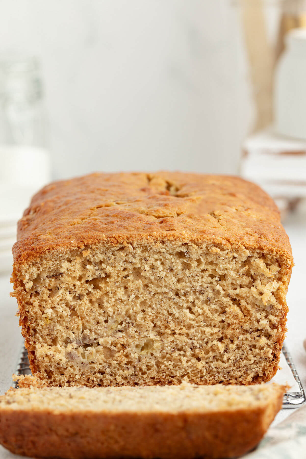 Sourdough banana bread on a cooling rack with a piece sliced off of the loaf.