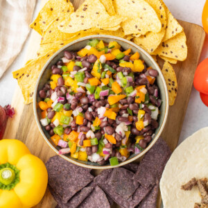 Mango black bean salsa in a bowl on a cutting board with chips and bell peppers.