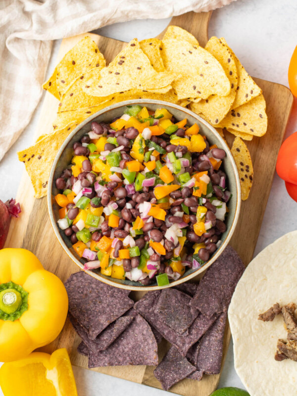 Mango black bean salsa in a bowl on a cutting board with chips and bell peppers.