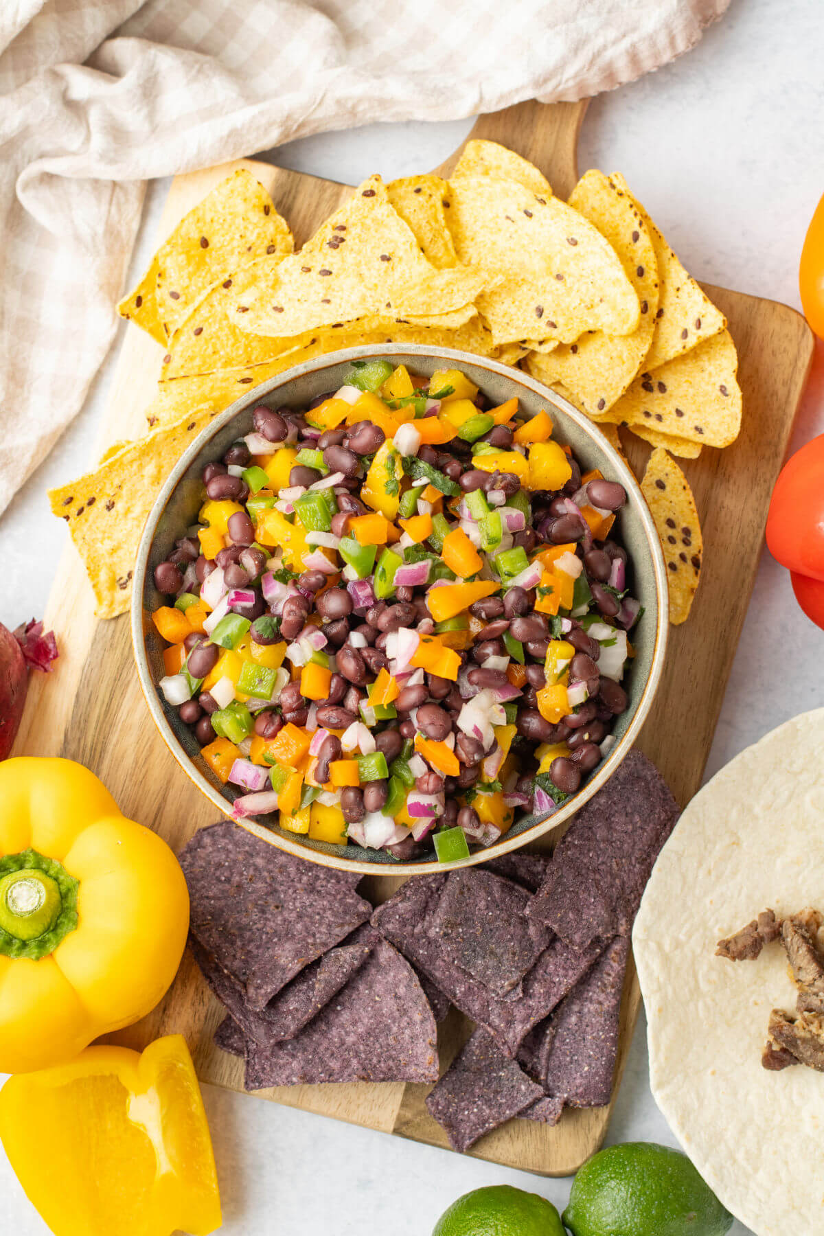 Mango black bean salsa in a bowl on a cutting board with chips and bell peppers.