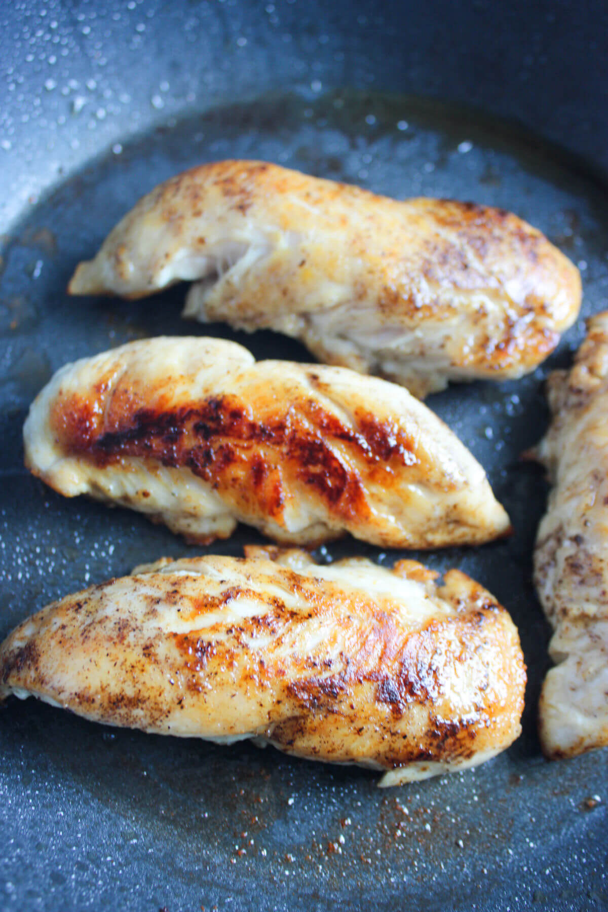 Chicken being cooked in a skillet for one pan chicken and vegetables recipe.