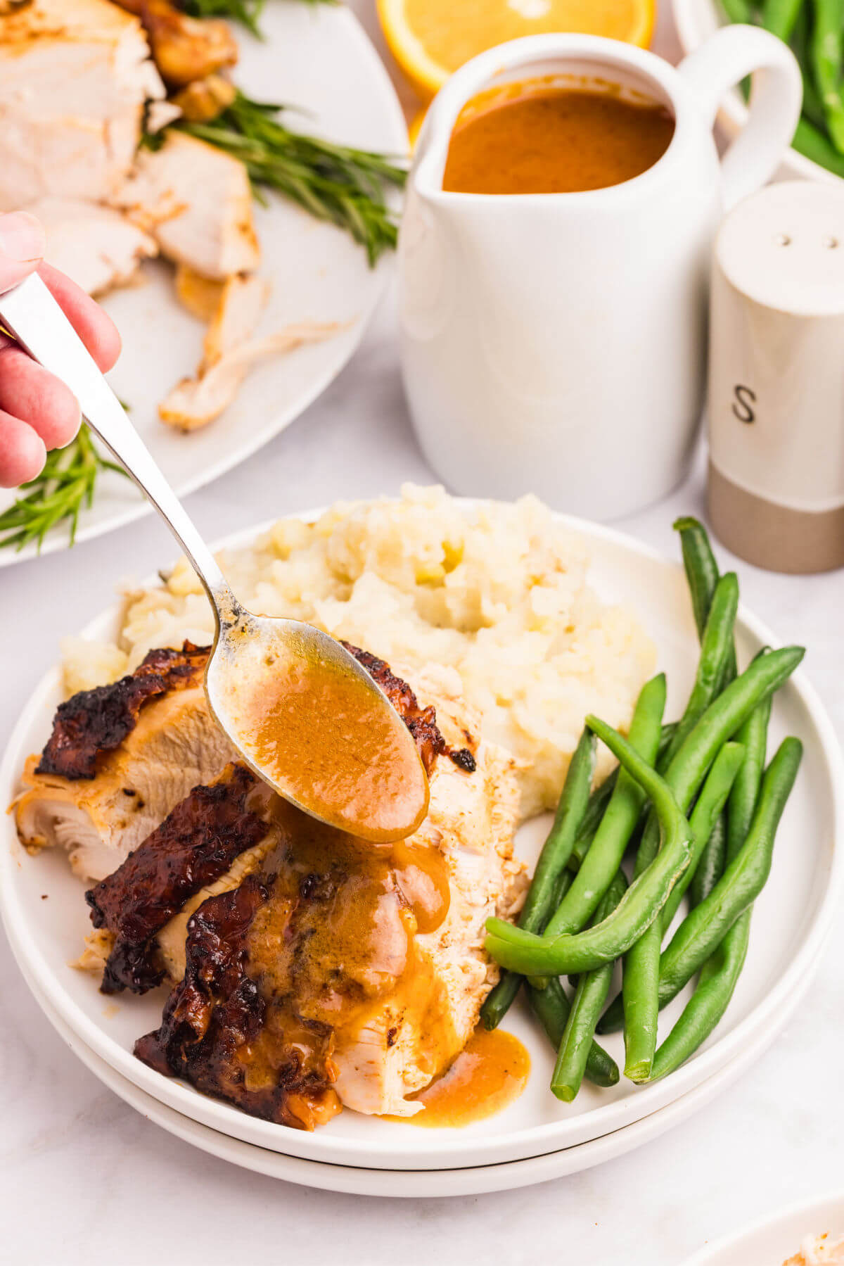 Plate full of turkey slices, mashed potatoes, and green beans, and gravy being drizzled over the turkey.