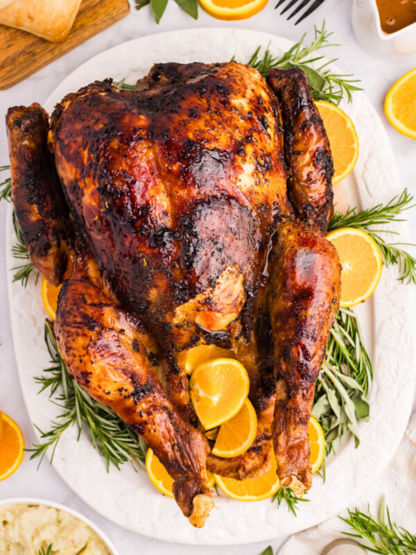 Orange glazed turkey on a white platter surrounded by herbs and orange slices.