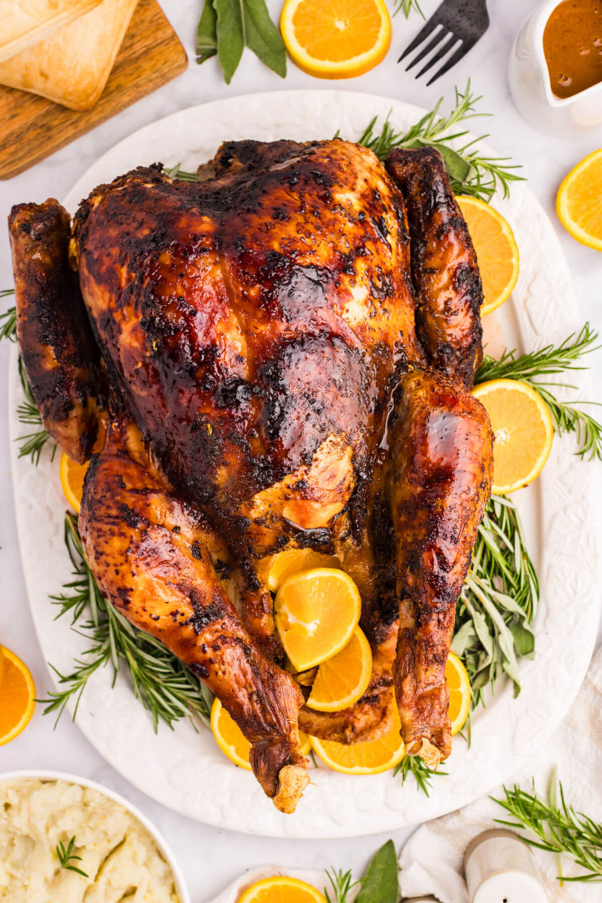 Orange glazed turkey on a white platter surrounded by herbs and orange slices.