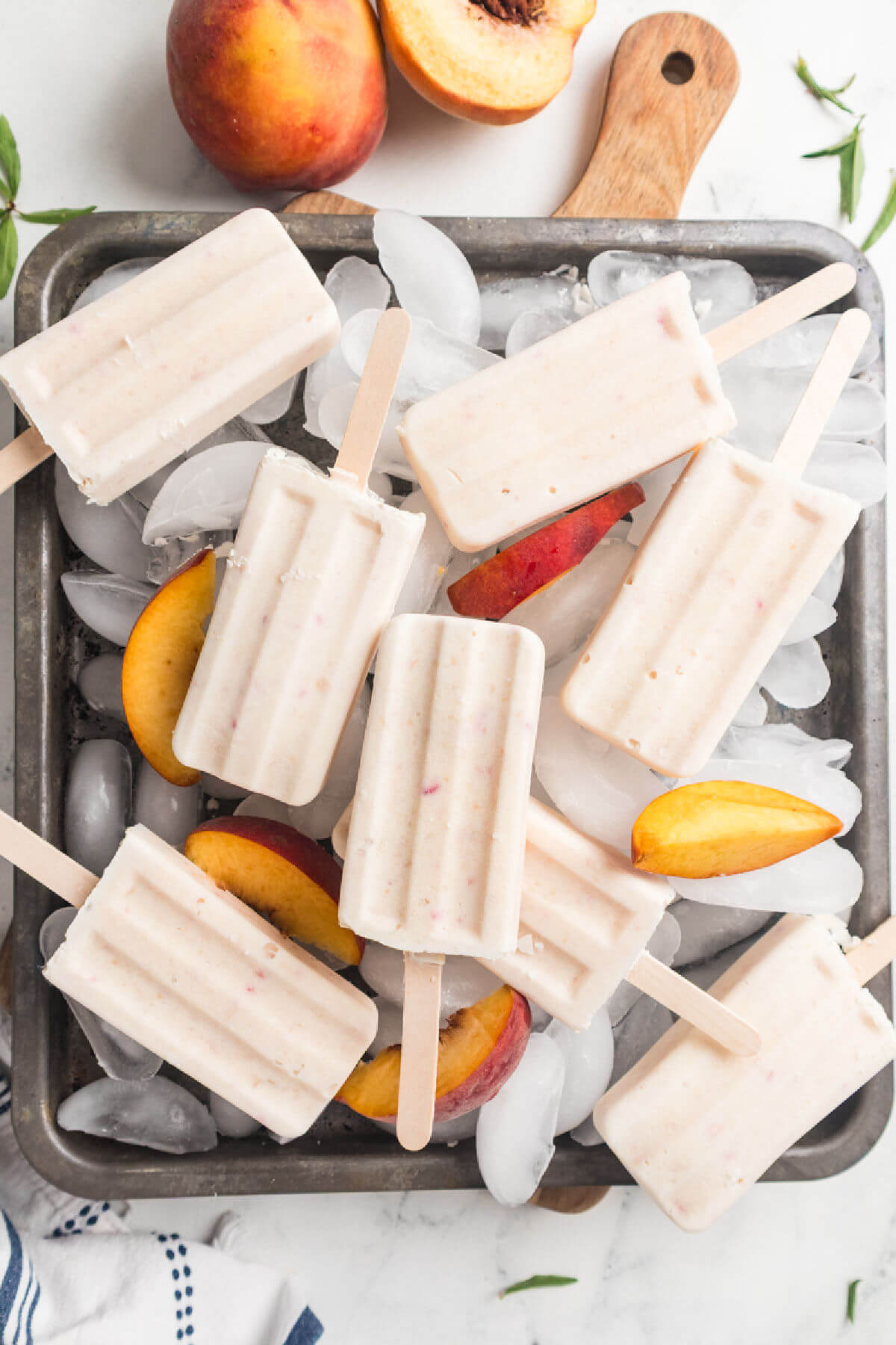 Peaches and cream popsicles on a baking pan with ice cubes.