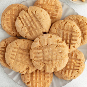 Peanut Butter Sourdough Cookies piled on a plate, with shelled peanuts to the side.