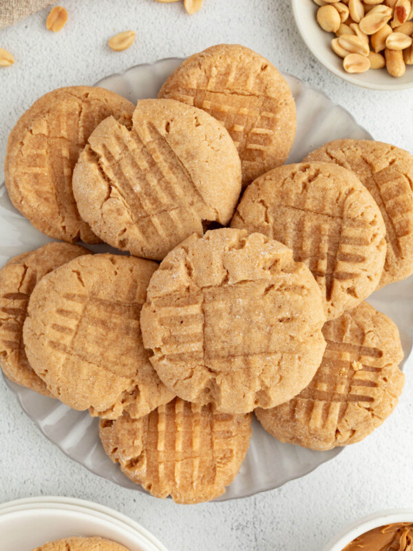 Peanut Butter Sourdough Cookies piled on a plate, with shelled peanuts to the side.