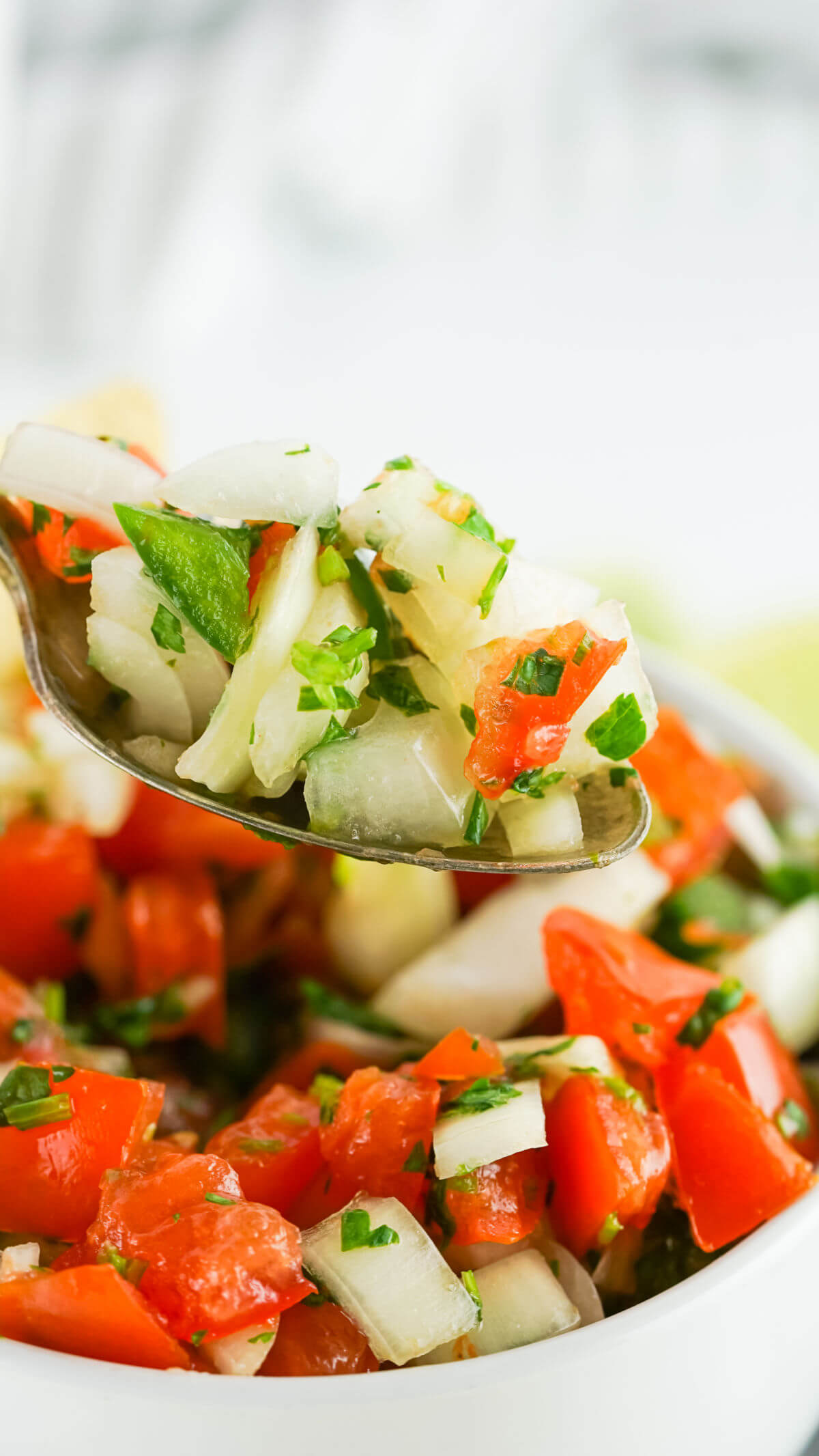 Homemade pico de gallo on a spoon being lifted out of mixing bowl.