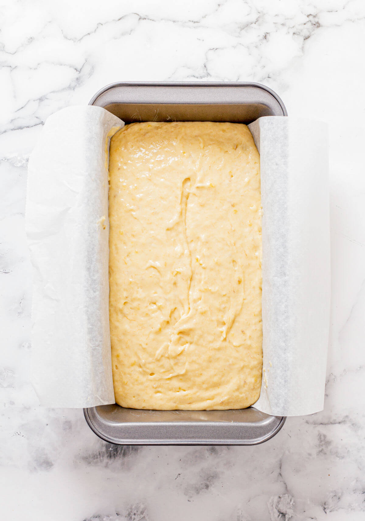 Bread pan with parchment and quick and easy banana bread batter ready to go into the oven.
