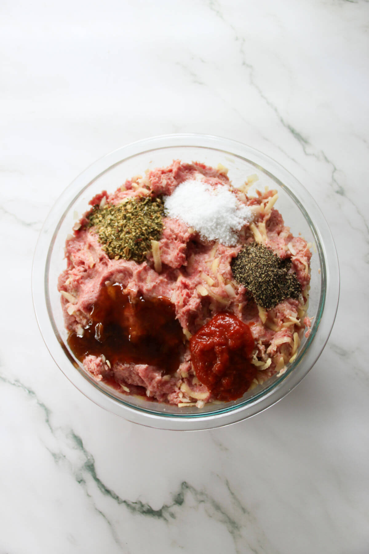 A mixing bowl showing the ingredients for savory meatballs being mixed together.