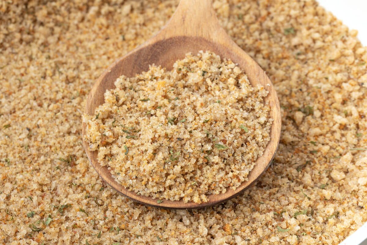 Seasoned breadcrumbs being stirred with a wooden spoon.