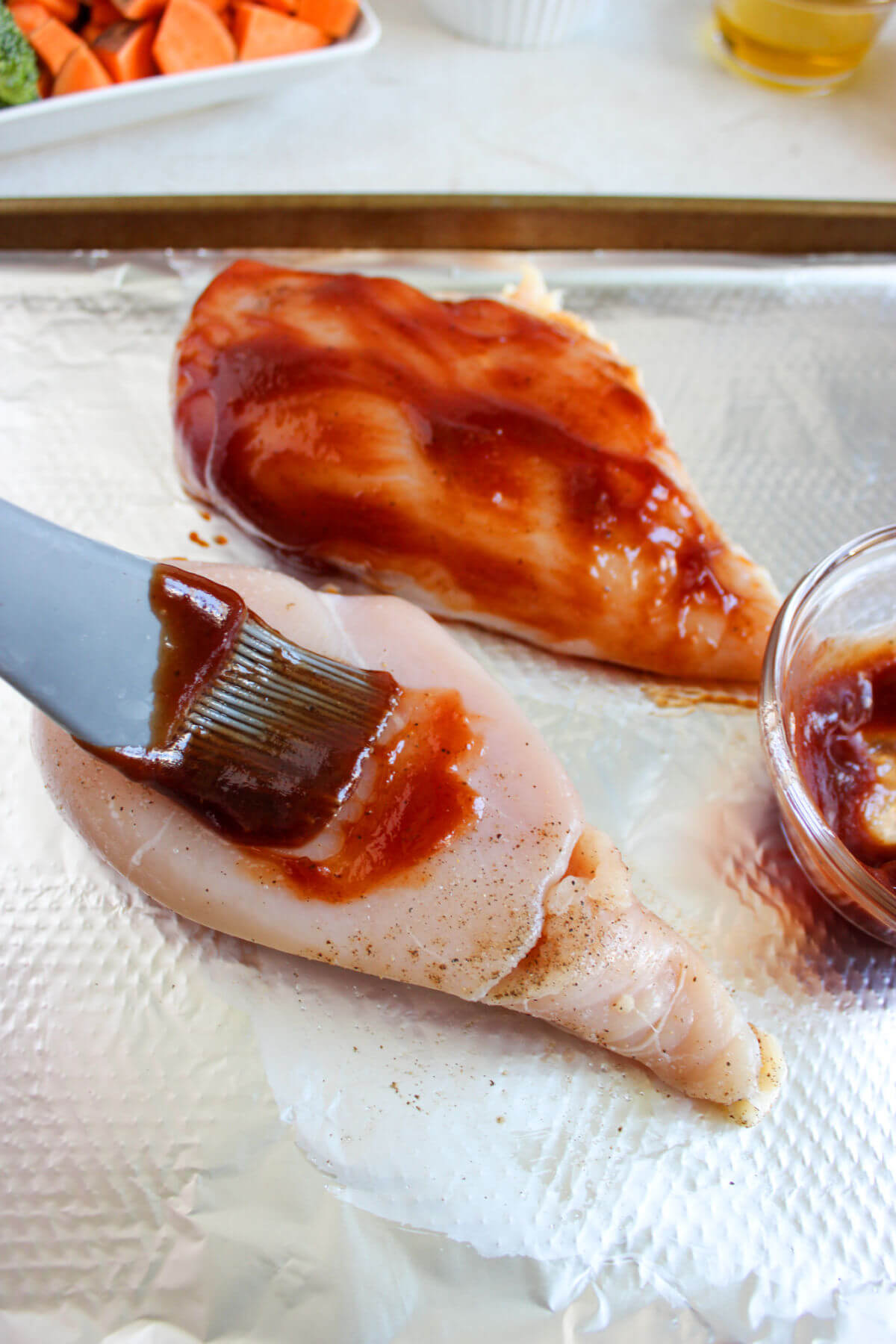 Chicken pieces with bbq sauce being painted on them.