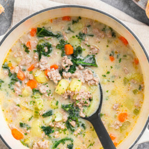 Dutch oven filled with tuscan sausage soup and a spoon stirring the soup.