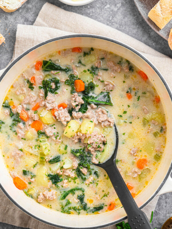 Dutch oven filled with tuscan sausage soup and a spoon stirring the soup.