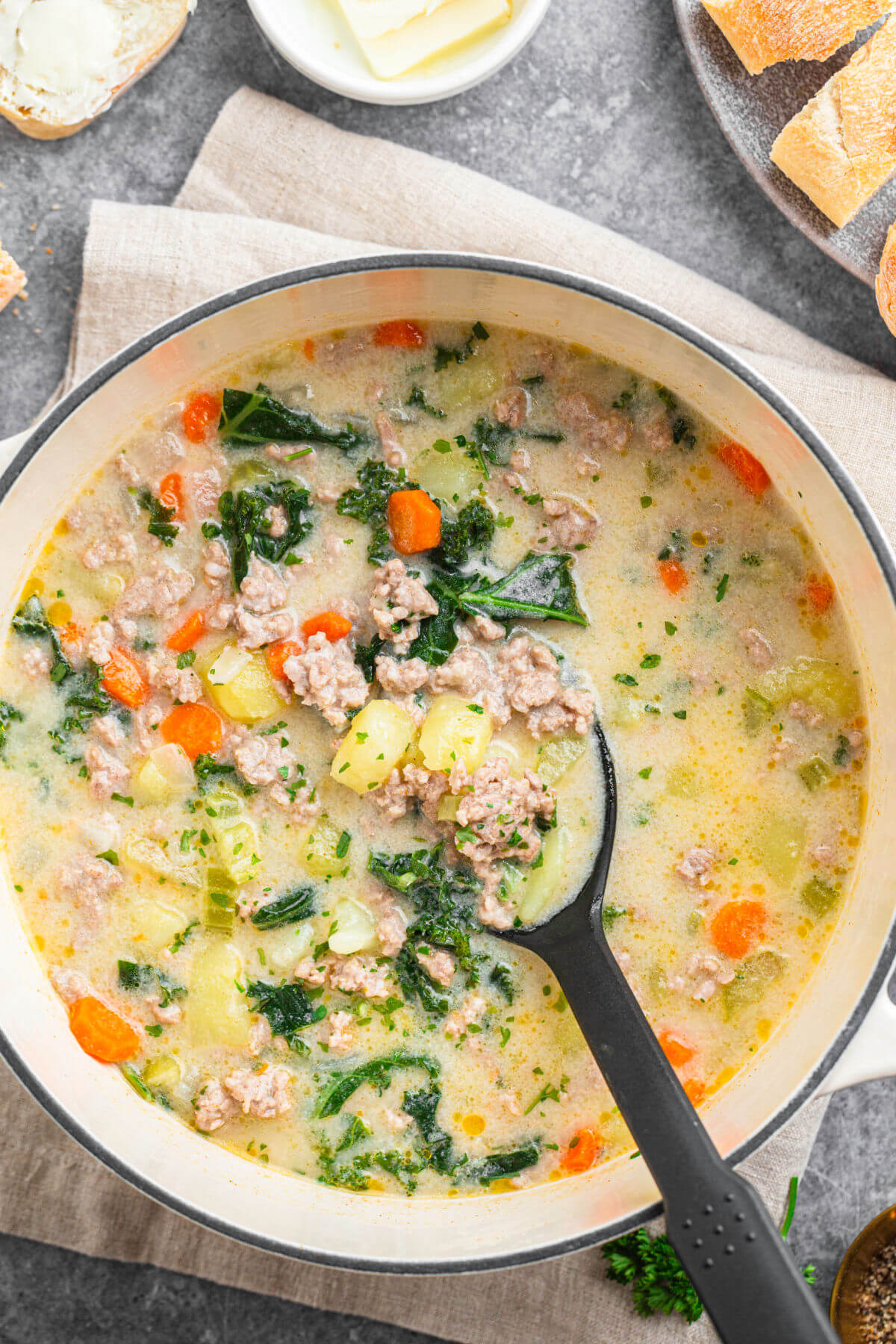 Dutch oven filled with tuscan sausage soup and a spoon stirring the soup.