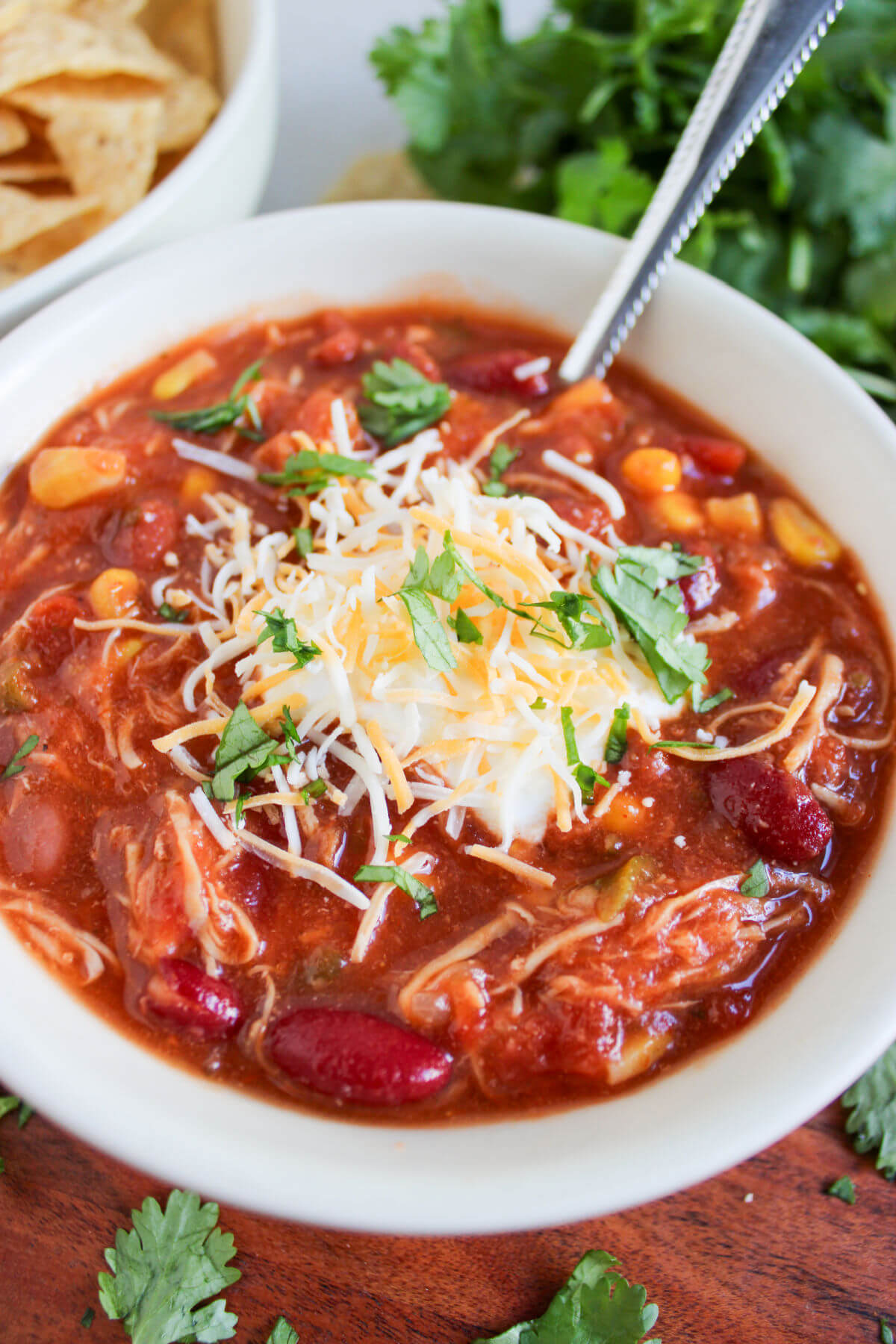 Slow cooker chicken taco chili in a bowl with parsley, cheese, and tortilla chips.