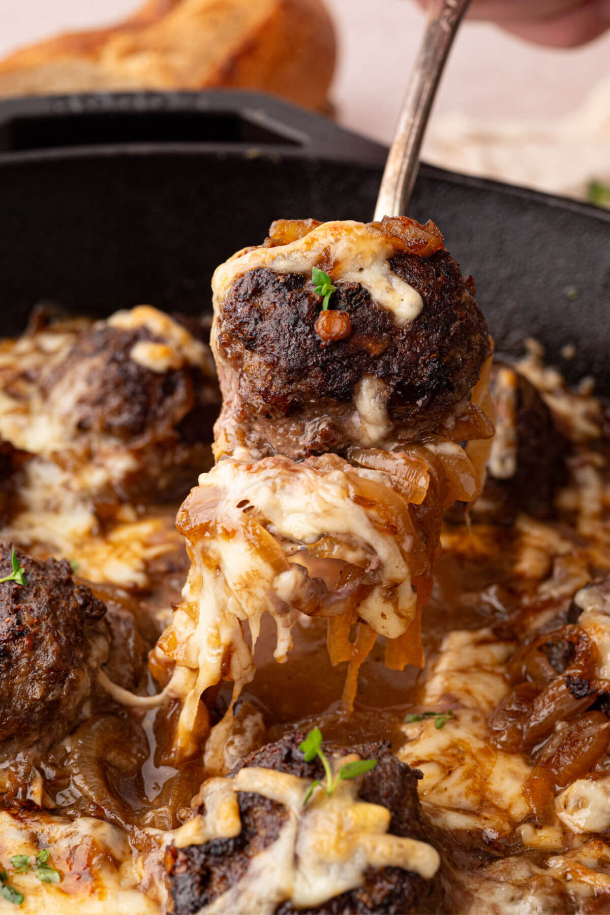 French onion meatballs in a cast iron skillet with a spoon lifting a meatball out of the pan.