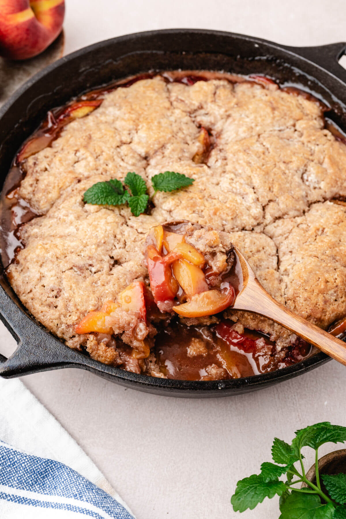 Cast iron skillet peach cobbler being served with a wooden spoon.