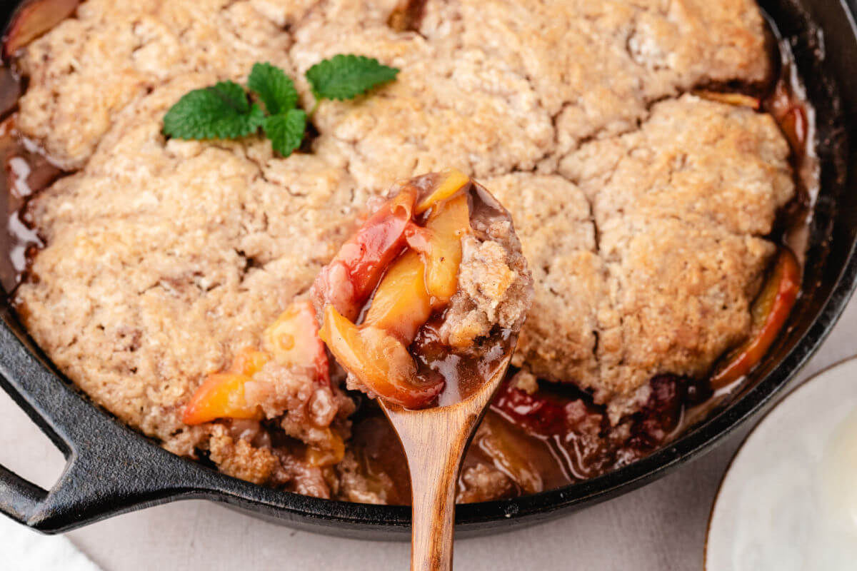 Skillet peach cobbler with a wooden spoon.