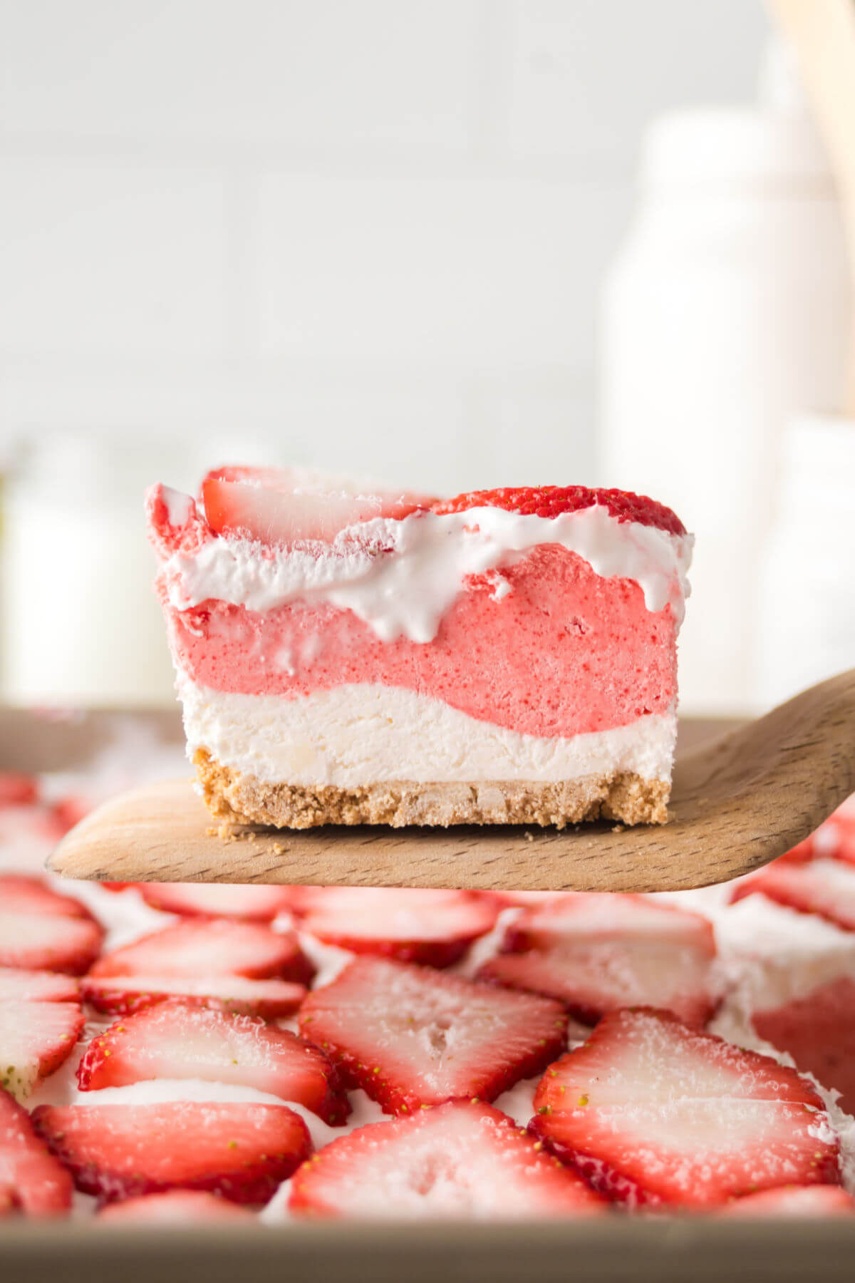 Strawberry delight recipe cut into a square on a wooden spatula.