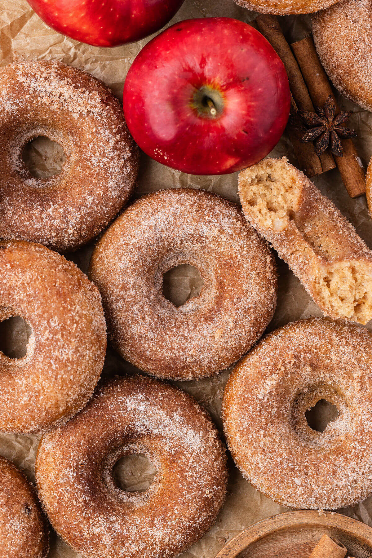 A pile of sourdough apple cider donuts next to a couple of apples.