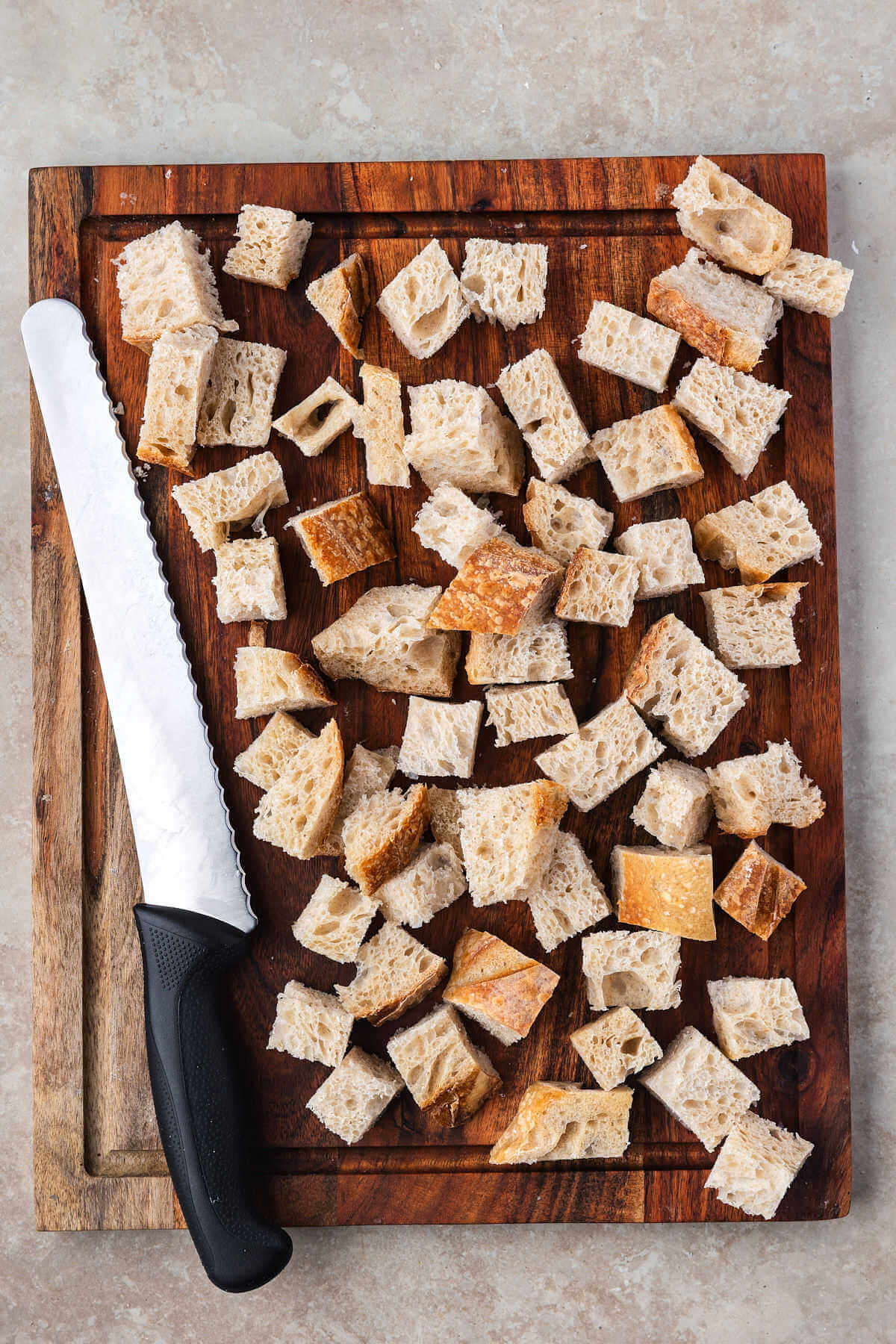 Bread cubes on a wood cutting board with a knife for sourdough breadcrumbs.