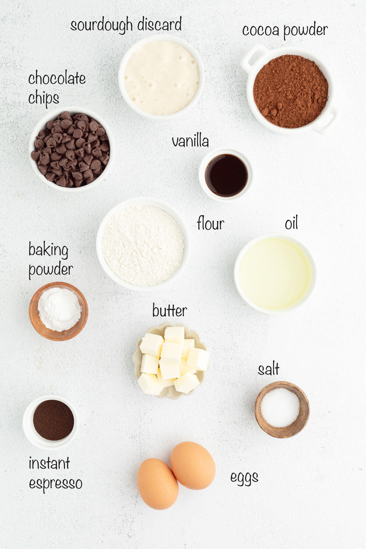 Sourdough brownies ingredients in small bowls with text overlay labeling each ingredient.
