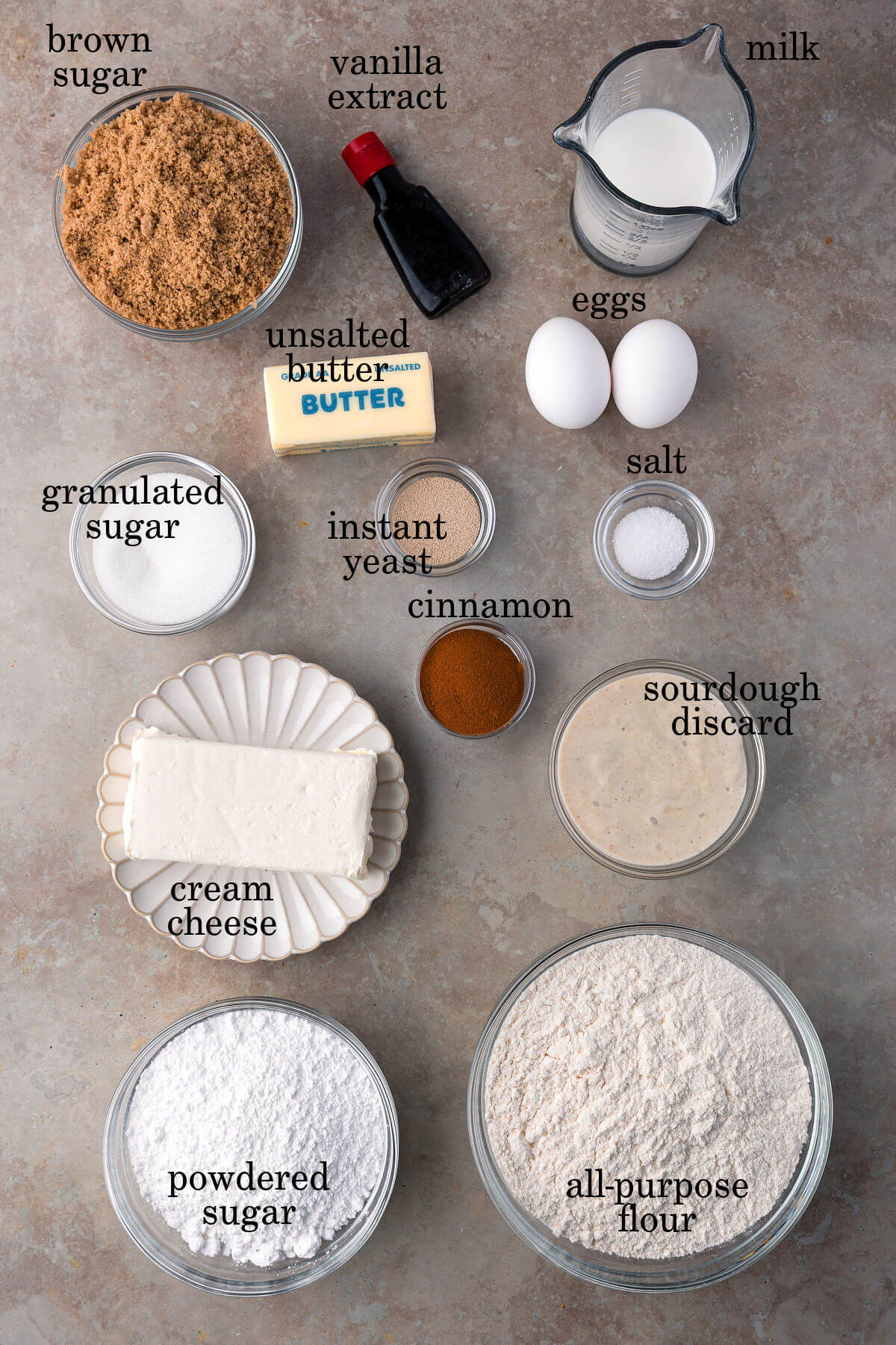Ingredients for sourdough discard cinnamon rolls in small bowls with text overlay labeling each ingredient.