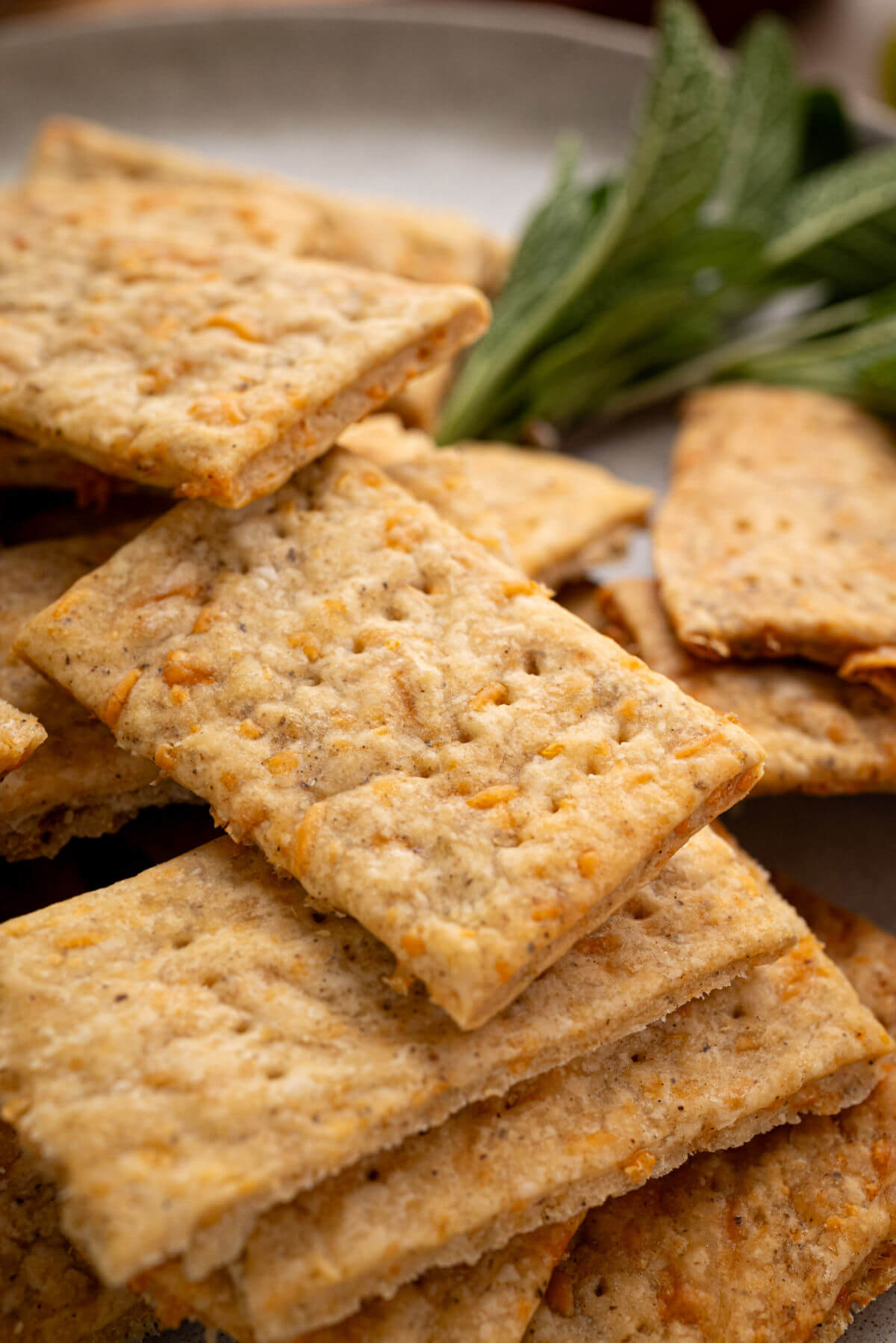 Sourdough discard crackers in a pile with fresh sage leaves.