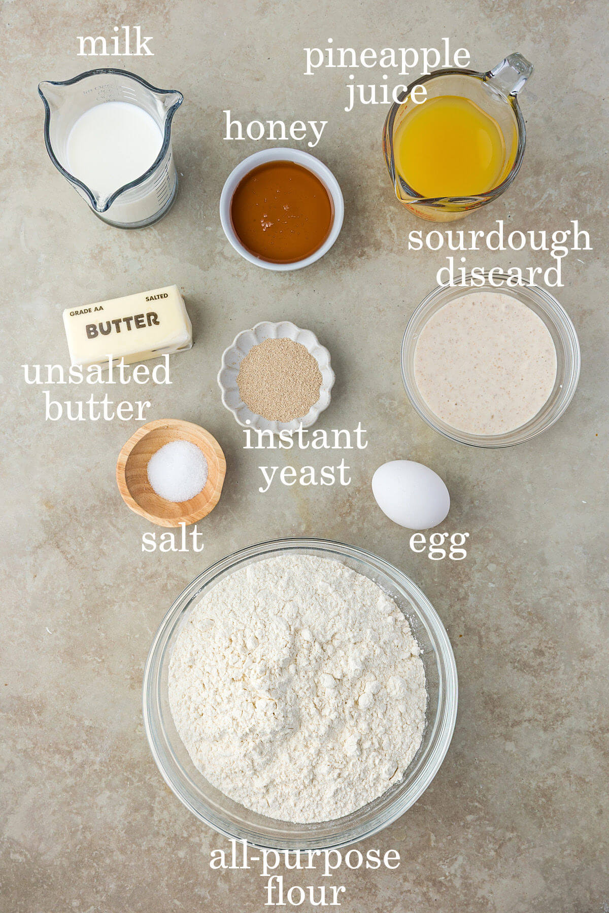 Ingredients for sourdough discard Hawaiian rolls in small bowls with labeled text overlay labeling each ingredient.