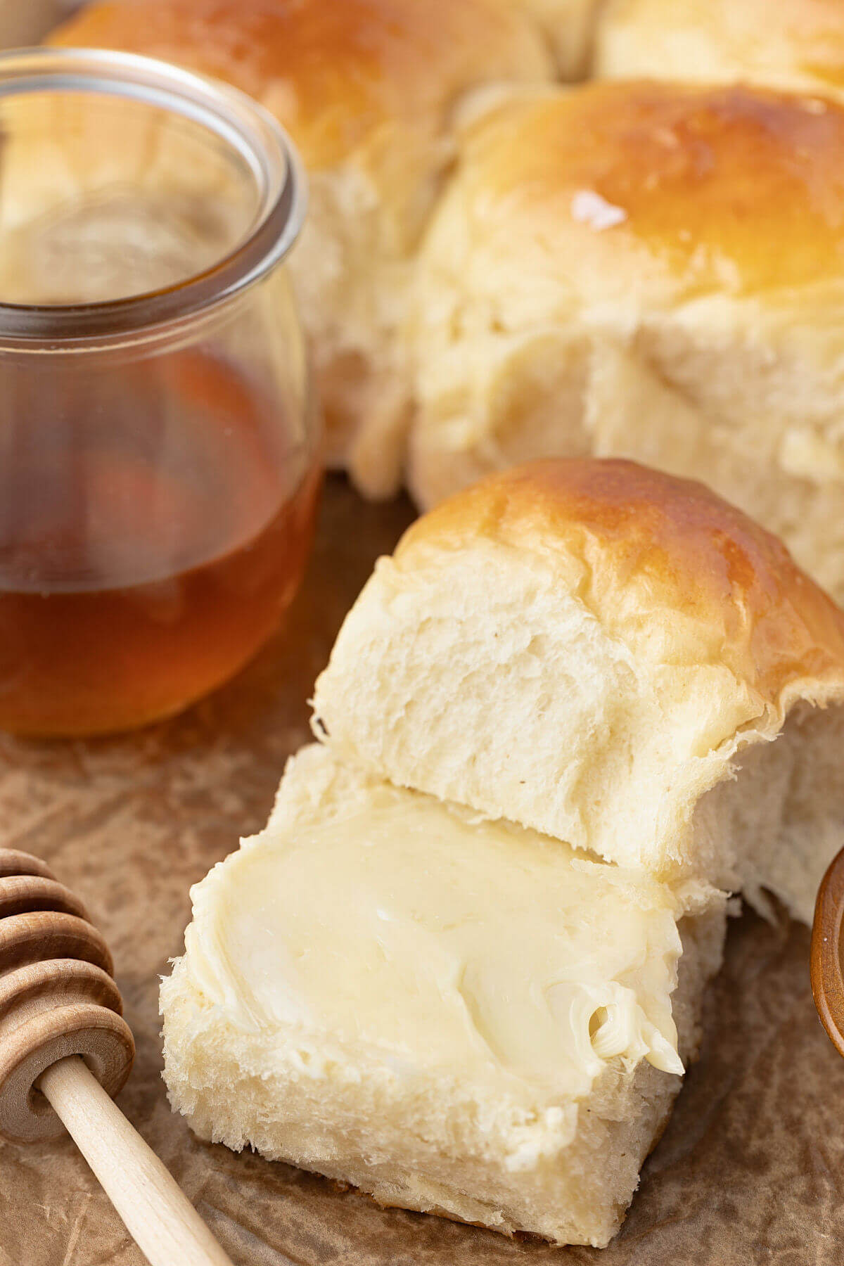 Freshly baked sourdough Hawaiian roll with butter on it, sitting next to a container of honey.